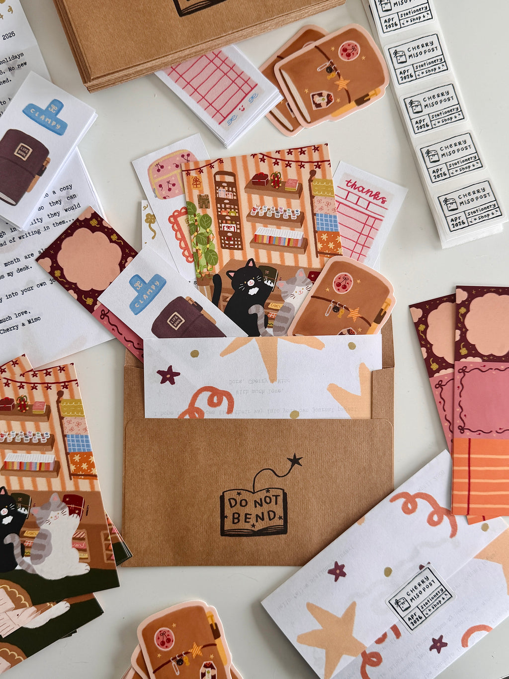 Flat lay of an envelope and various stationery items from the April edition of Cherry Miso Post peeking out, including an illustrated postcard, stickers, memo pages, and paper scraps with whimsical designs.