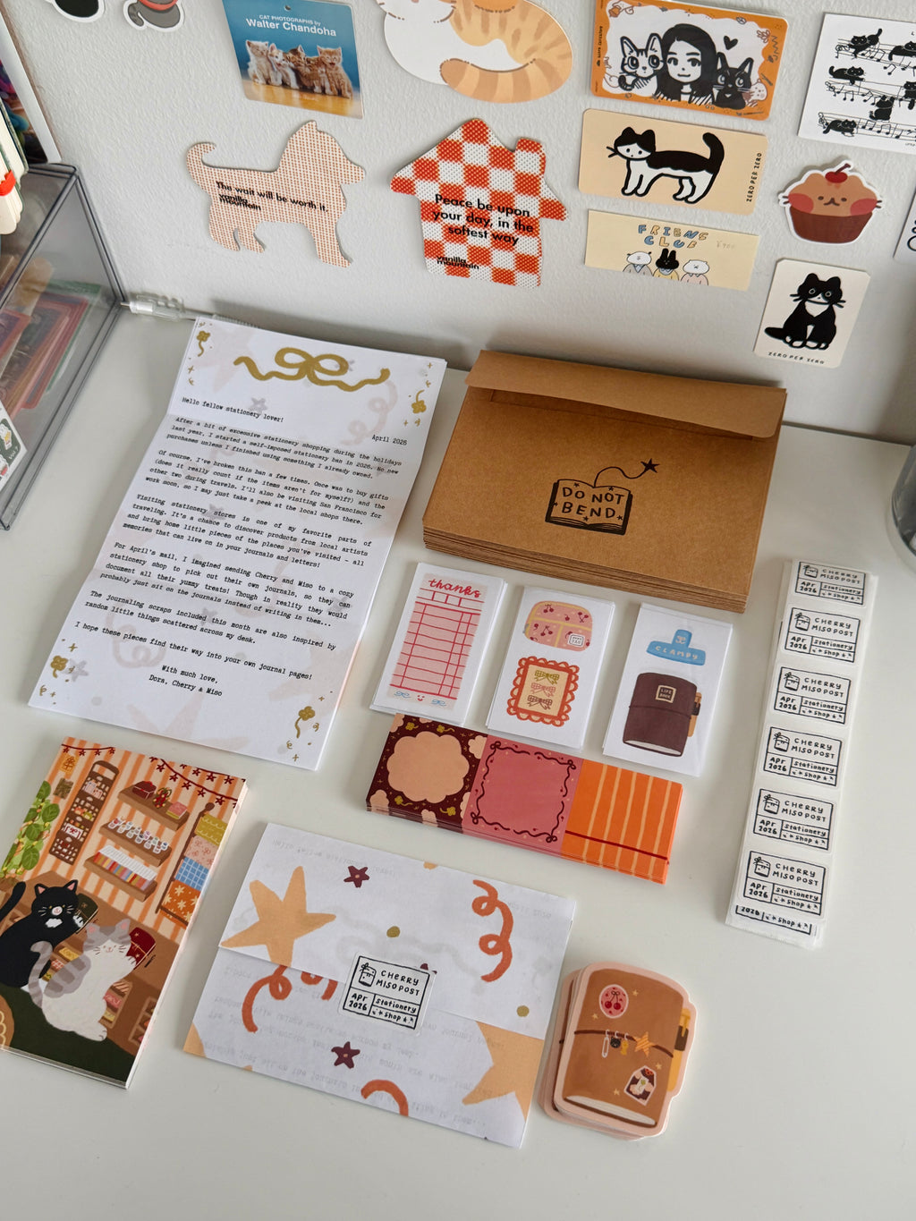 Flat lay of stacks of stationery items including a letter, envelopes, decorative stickers, and paper bookmarks arranged neatly on a desk, ready to be packed.