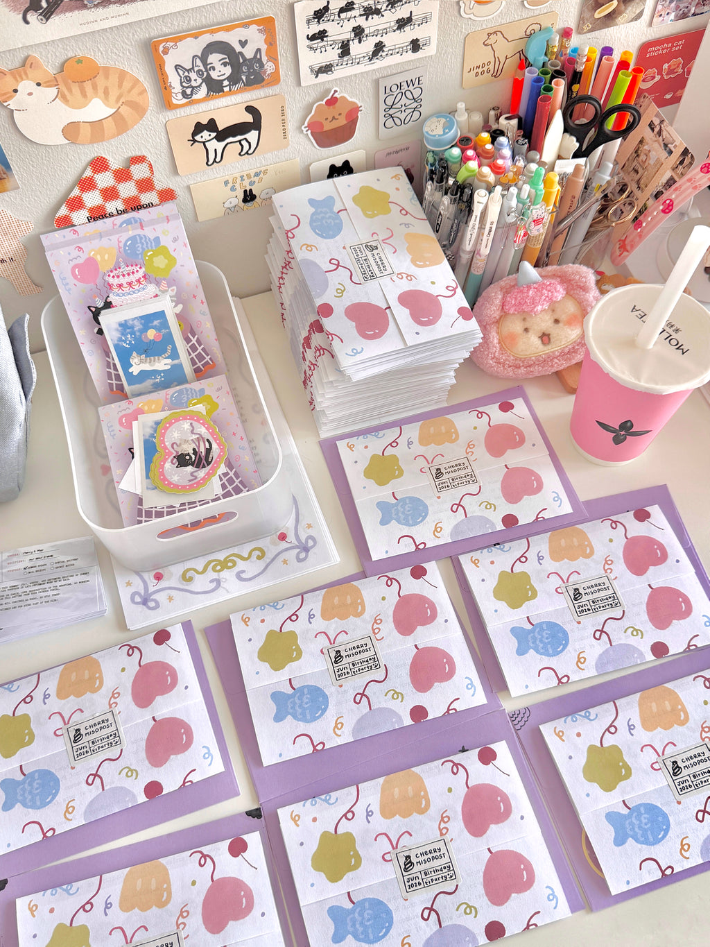 Light purple envelopes spread out on a white desk, with wrapped letters resting on top, featuring colorful balloon illustrations.