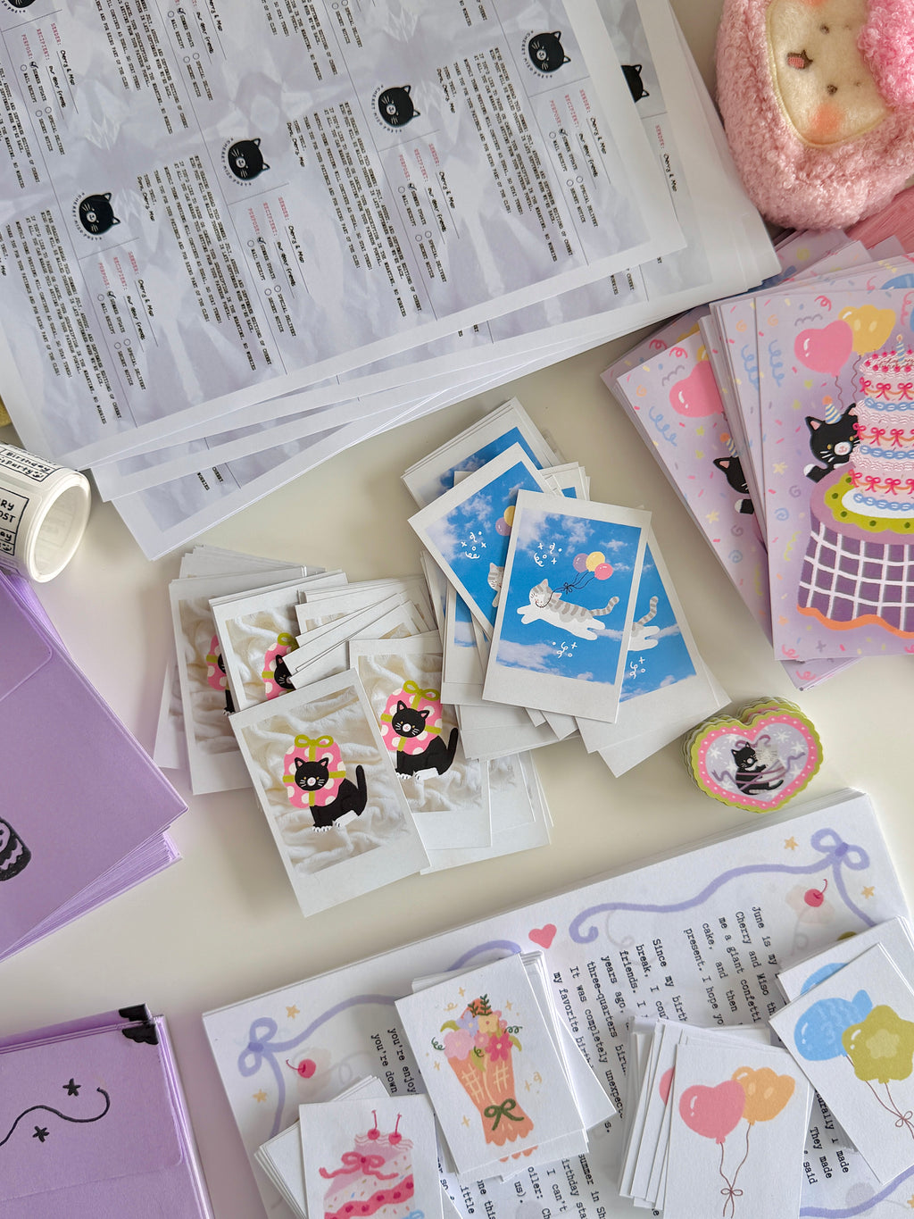 A flatlay on a white table with stacks of postcards, polaroid cards, stickers, letters, and purple envelopes.