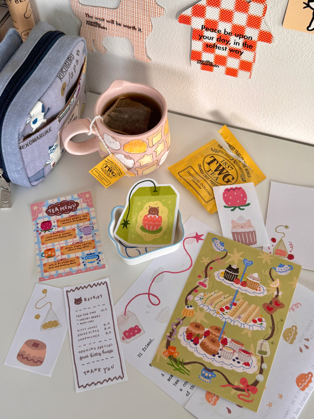 Flat lay of colorful paper stationery from the March edition of Cherry Miso Post featuring cute desserts and tea-themed designs, alongside a pink mug filled with tea.