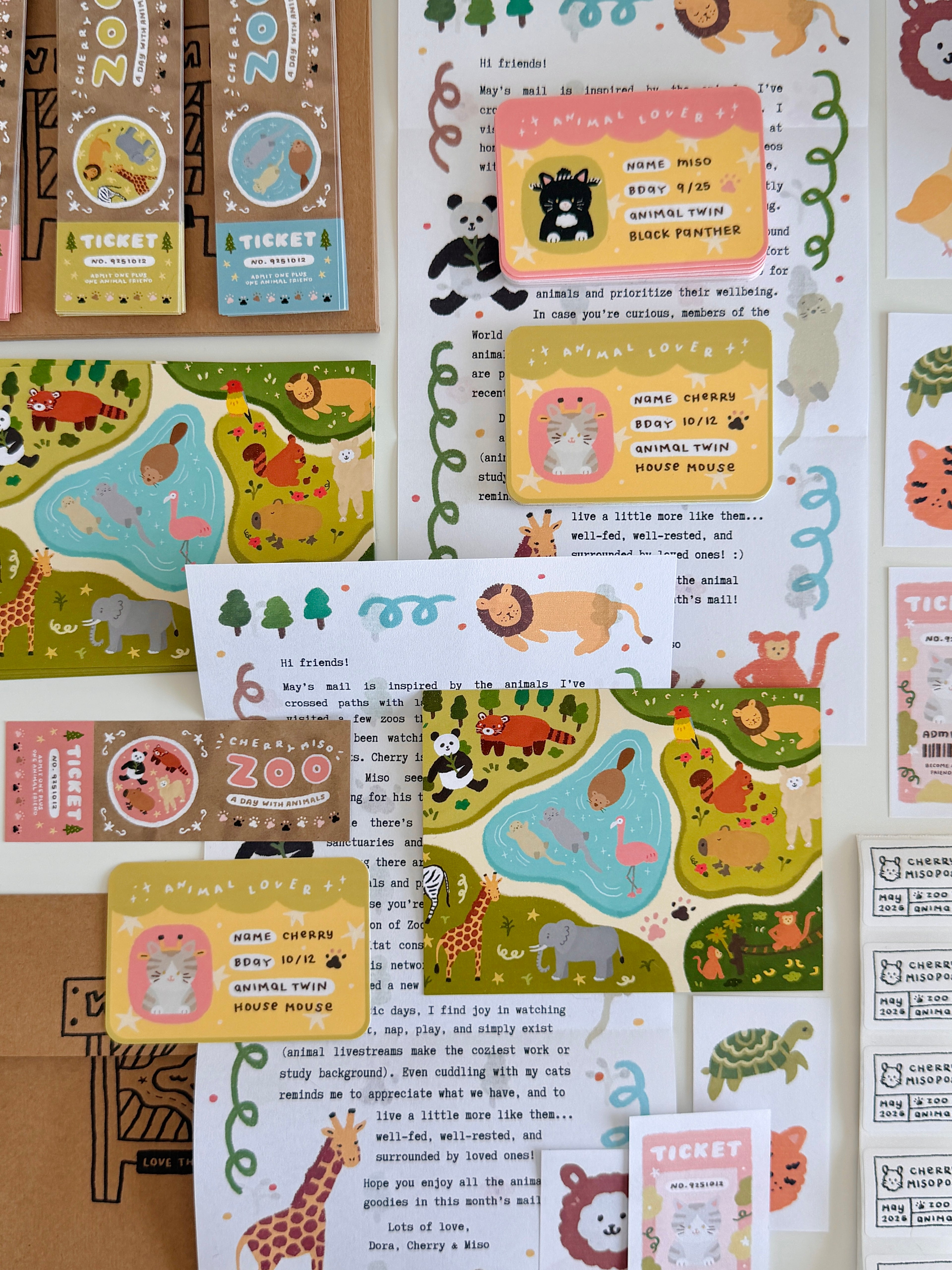 Flat lay of colorful stationery items featuring illustrated zoo animals, postcards, tickets, and cards with playful designs, part of the May edition of Cherry Miso Post.