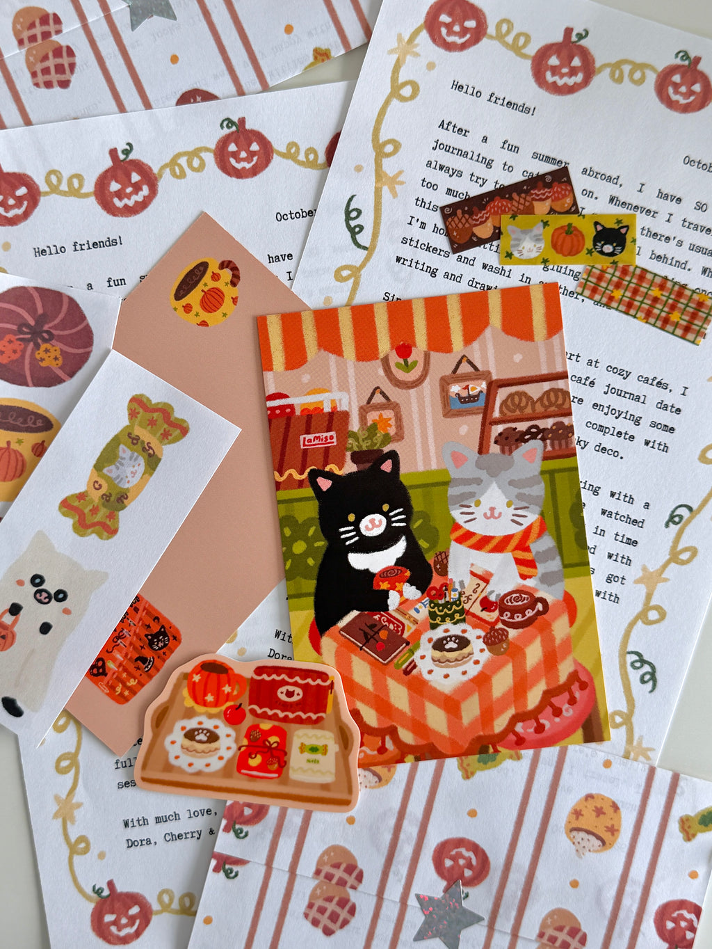 A flatlay on a white table of cat and fall-themed stationery items, including a letter, postcard, sticker, washi stickers, paper scraps, and an envelope.