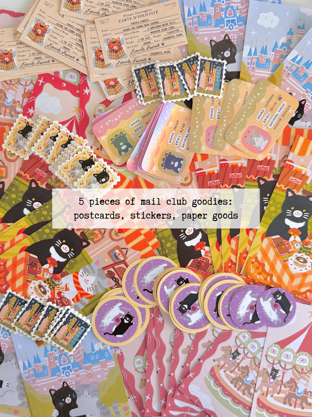 A flatlay of piles of cat-themed stationery items, including postcards, stickers, paper scraps, washi tape, and stamp stickers