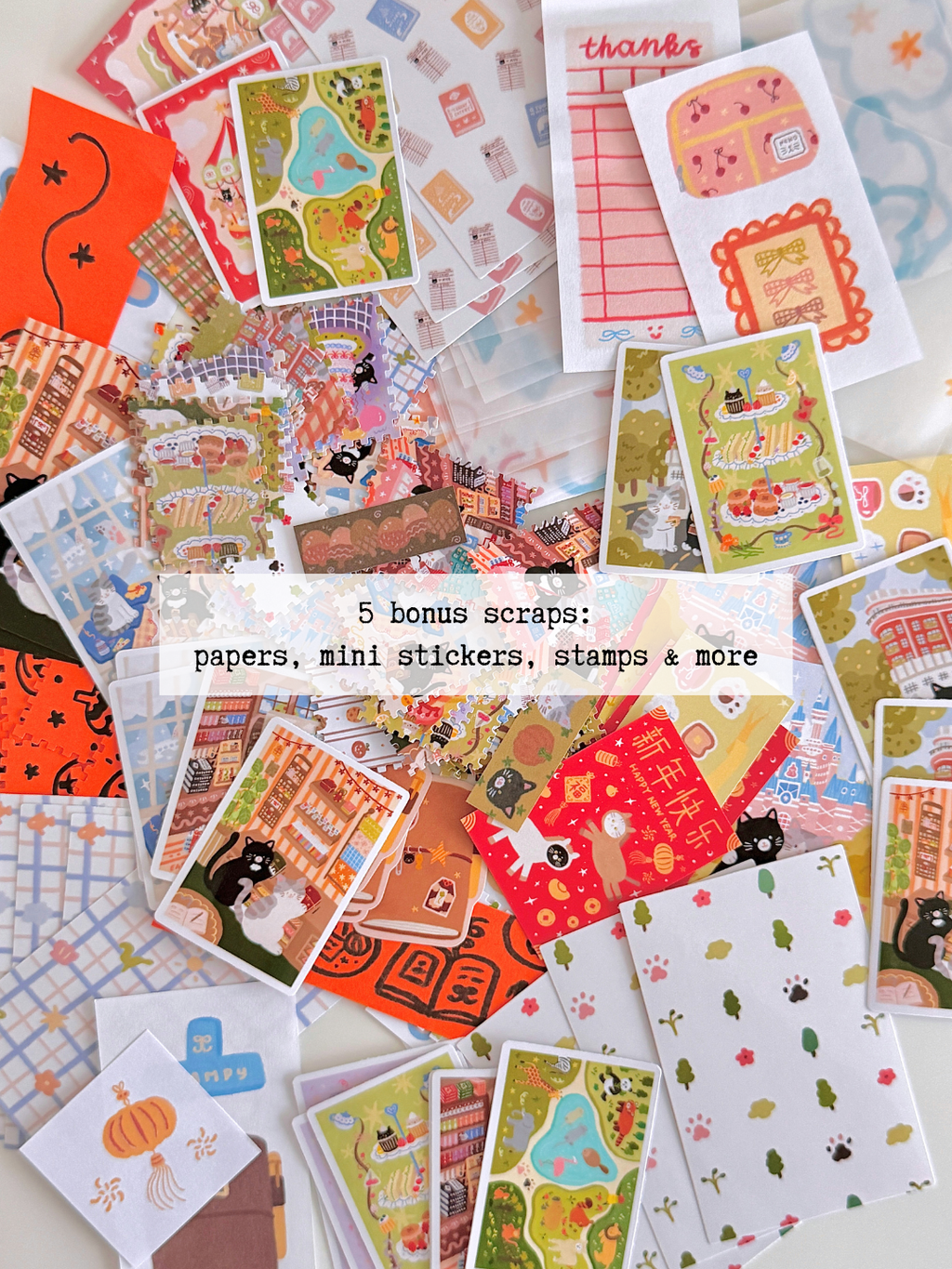 A flatlay of piles of cat-themed stationery items, including postcards, stickers, paper scraps, washi tape, mini stamps, and colored paper